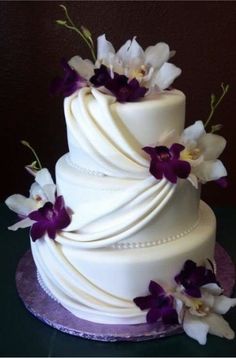 a three tiered white wedding cake with purple orchids