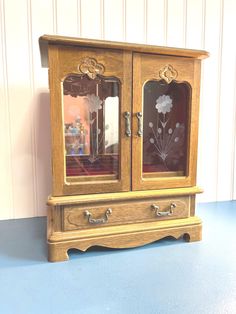 a wooden cabinet with two glass doors on the top and bottom, sitting on a blue surface