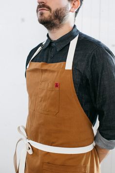 a man with an apron on standing in front of a white wall