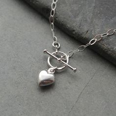 "This sterling silver necklace features a sterling silver heart charm and has a T bar clasp for front fastening It is made from flat oval sterling silver trace chain The sterling silver filled heart charm is hollow and measures 10 mm. The t-bar measures 18 mm with the ring having a 10 mm outside diameter Available in  a choice of 14\", 15\", 16, 18  or 20 inch sterling silver chain. A Lovely everyday wear necklace. Lovely gift for a loved one. The necklace will arrive in a gift box." Silver Heart Necklace With Toggle Clasp For Gift, Silver Heart Toggle Necklace For Gift, Silver Heart Toggle Necklace As Gift, Sterling Silver Heart Necklace With Toggle Clasp, Heart Shaped Sterling Silver Necklace With Toggle Clasp, Silver Heart Pendant Toggle Necklace, Silver Heart Charm Toggle Necklace For Valentine's Day, Silver Toggle Necklace With Heart Charm For Valentine's Day, Silver Heart Toggle Necklace With Lobster Clasp