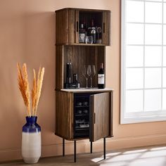 a cabinet with wine glasses and bottles in it next to a vase filled with dry grass