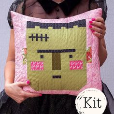 a woman holding up a pillow made to look like a cat with pink and black squares