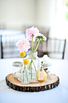 flowers in mason jars sitting on top of a wooden slice that has been placed on a table