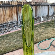 a green vase sitting on top of a glass table next to a garden hose holder