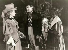 an old black and white photo of three people dressed in period clothing talking to each other