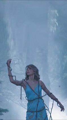 a woman in a blue dress is holding two ropes and looking up at the sky