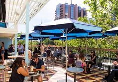 people sitting at tables under blue umbrellas on a sunny day