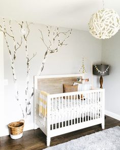 a white crib in the corner of a room with a tree painted on it