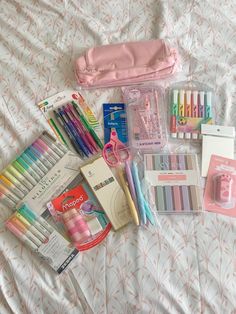 the contents of an organized travel bag laid out on a bed, including pens, pencils and markers