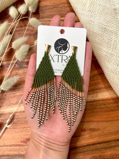 a pair of green tasseled earrings sitting on top of a wooden table next to some dried grass