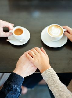 two people holding hands over a table with cups of coffee and saucers on it