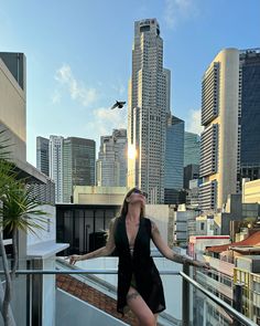 a woman standing on top of a balcony in front of tall buildings with her arms outstretched