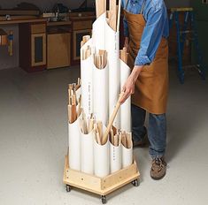 a man in an apron standing next to a large stack of pipes with wooden handles