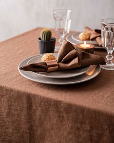 the table is set with silver plates and brown napkins, glass vases and cactus