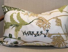 a white pillow with green and gold designs on it sitting on a chair next to a wall