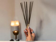 a person holding up some sticks in front of a lit candle on a table next to a wall