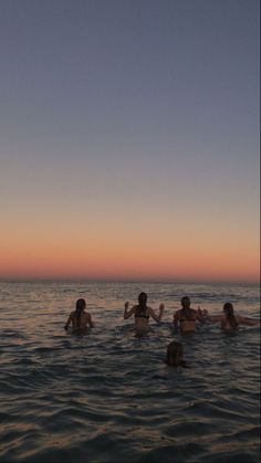 four people swimming in the ocean at sunset or dawn, with one person holding his hand up