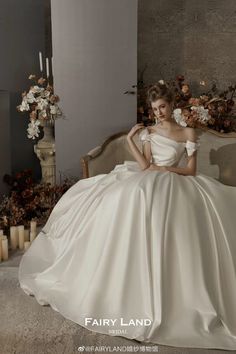 a woman in a white dress sitting on a couch with candles and flowers behind her