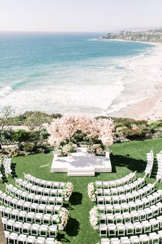 an outdoor ceremony set up with white chairs and flowers on the lawn next to the ocean