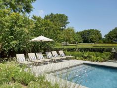 an outdoor swimming pool with lounge chairs and umbrellas next to it in the garden