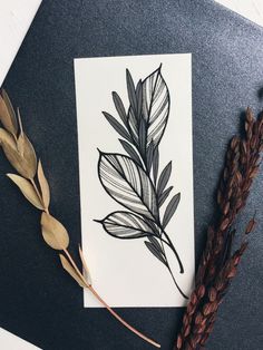 a piece of paper with leaves on it next to some dried grass and brown stalks