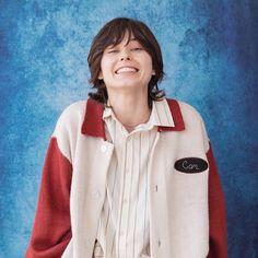 a young man is smiling and wearing a white jacket with red sleeves on his shoulders