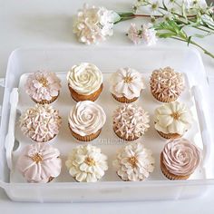 cupcakes decorated with pink and white frosting on a tray next to flowers