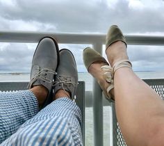 two people are sitting on a balcony overlooking the ocean with their feet propped against each other