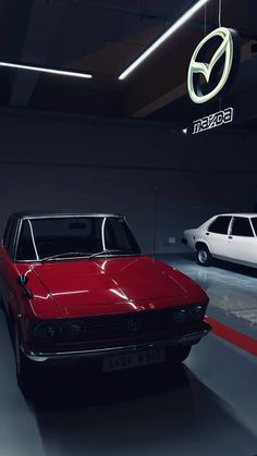 two cars are parked in a garage with the mazda logo on the wall behind them