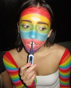 a woman with her face painted like a rainbow holding a cell phone to her mouth