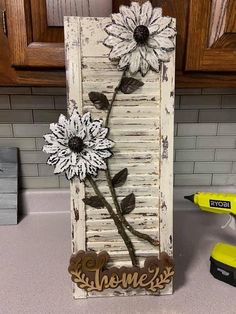 a wooden sign with flowers on it sitting next to a yellow blow dryer in a kitchen