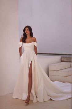 a woman in a white dress standing next to a wall with her leg up on the ground