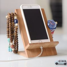 a cell phone on a wooden stand with bracelets around it and a watch in the background