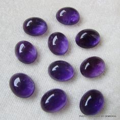 six purple glass cabochons sitting on top of a white cloth