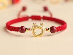 a red string bracelet with a gold plated ring and beaded beads on it