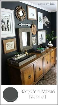 a black wall with pictures on it and various framed objects above the dresser in this living room