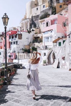 a woman in a white dress is walking down the street with her hair blowing in the wind