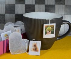 a coffee cup sitting on top of a table next to small pictures and tags hanging from it's sides