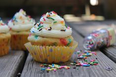 several cupcakes with white frosting and sprinkles on a wooden table