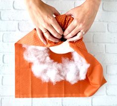 someone is holding an orange paper bag with white clouds on it, and there are two hands reaching for the fabric