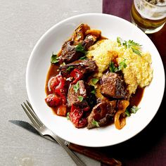 a white plate topped with meat and veggies next to a glass of beer