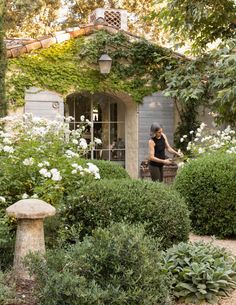 a woman standing in front of a house surrounded by bushes