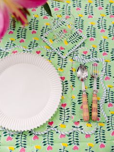 an empty plate and utensils on a floral table cloth with pink flowers in the background