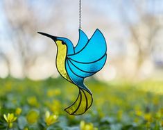 a blue and yellow bird hanging from a chain in a field full of green flowers