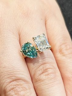 a woman's engagement ring with two emeralds and diamonds on her finger,