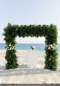 an outdoor ceremony setup on the beach with flowers and greenery in front of the ocean