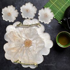 three white flowers sitting on top of a table next to a cup and saucer