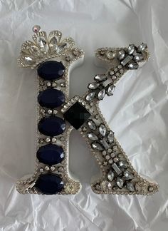 the letter k is decorated with blue and clear stones, surrounded by crystal jewels on a white background