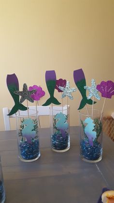 there are four little mermaid cupcake toppers in the vases on the table