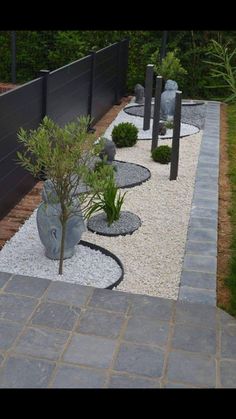 an outdoor garden with gravel, rocks and plants in the center is surrounded by black fencing